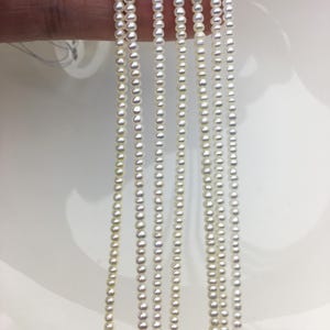 May include: A strand of white freshwater pearls, strung on a thin thread. The pearls are small and uniform in size, creating a delicate and elegant look.