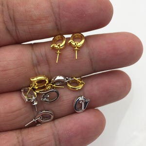 Pu&ograve; includere: Una collezione di componenti per orecchini in oro e argento. I componenti includono piccoli orecchini a cerchio con un perno per attaccare un ciondolo o una perla. Gli orecchini dorati sono di un giallo brillante, mentre quelli argentati hanno una finitura lucida.