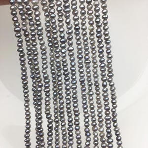 May include: Multiple strands of grey freshwater pearls. The pearls are small, oval-shaped, and have a lustrous sheen. The strands are held together, showcasing the pearls' colour variations, from light to dark grey. Suitable for jewellery making.