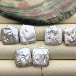 Puede incluir: Seis cabujones de perlas barrocas blancas, cada uno con una forma irregular única y un ligero brillo iridiscente. Las perlas están dispuestas en dos filas sobre una superficie blanca.