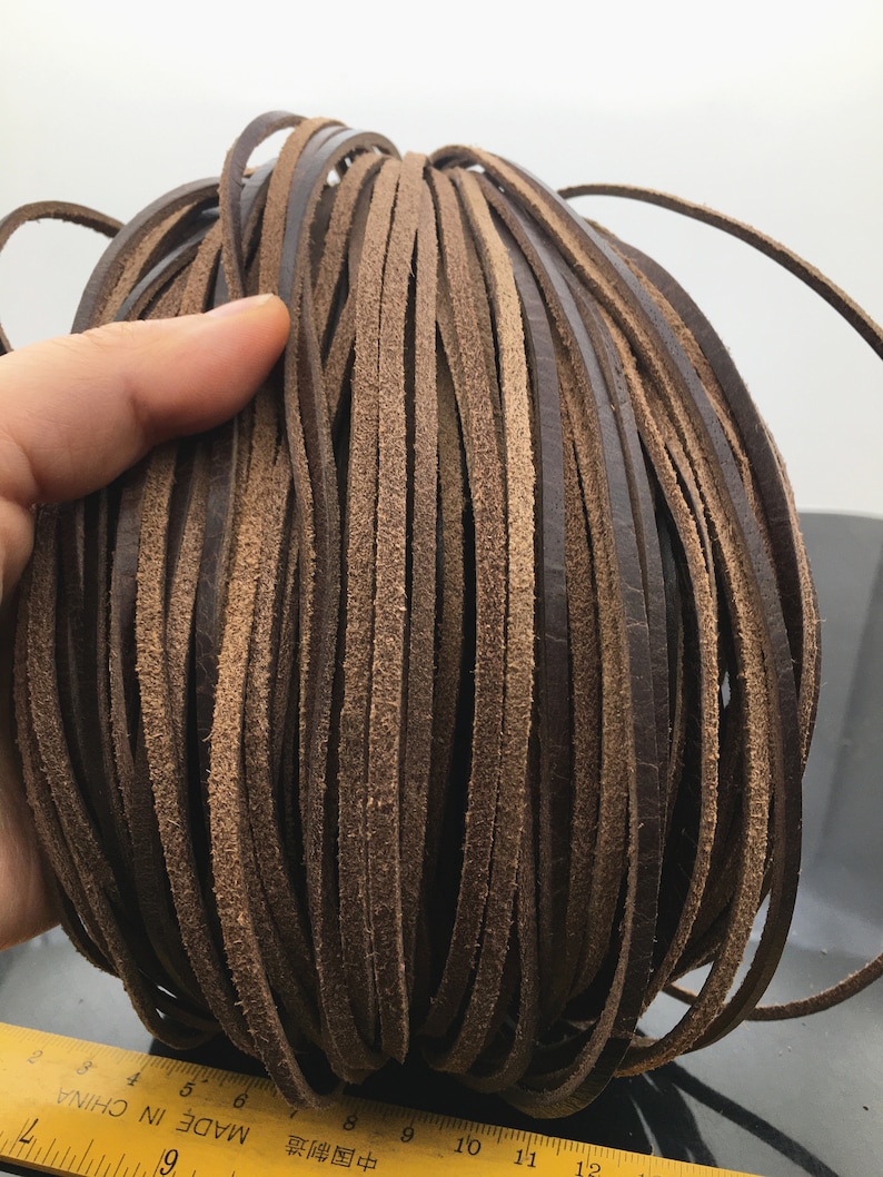 May include: A close-up of a bundle of brown leather cord. The cord is approximately 5/16 inch wide and is made in China.
