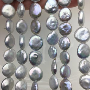 May include: A strand of white and iridescent freshwater pearls, each pearl is a flat, round disc shape.