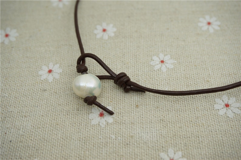 Puede incluir: Un collar sencillo de cuero marr&oacute;n con un solo colgante de perla blanca.