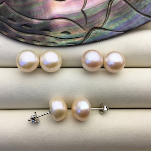 Könnte beinhalten: Ein Paar Perlenohrringe mit silbernen Stiften. Die Perlen sind in einem weichen, cremeweißen Farbton gehalten und haben eine runde Form.