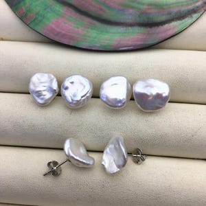 Puede incluir: Cuatro pendientes de perlas barrocas blancas con postes de plata. Las perlas son de forma irregular y tienen un acabado liso y brillante.