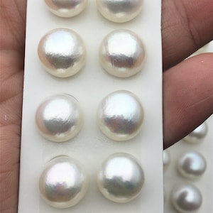 Puede incluir: Una hoja de cartulina blanca con 12 perlas redondas blancas dispuestas en filas. Las perlas son lisas y brillantes.