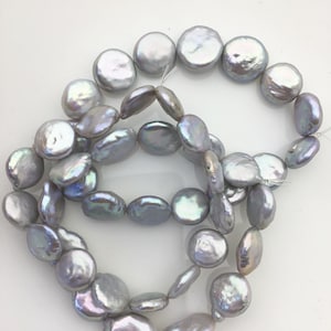 May include: Strands of iridescent, grey-toned, coin-shaped pearls. The pearls have a lustrous sheen and vary in size and shape, strung together on a clear thread. The pearls are a mix of round and oval shapes.