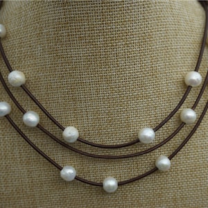 May include: A three-strand necklace with white pearls and brown leather cord.