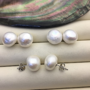 May include: Four pairs of white pearl earrings with silver posts. The pearls are round and have a smooth, glossy finish.
