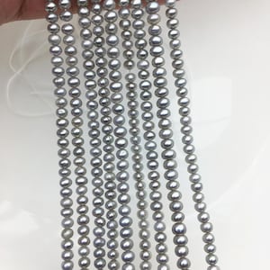 May include: Strands of gray pearls of varying sizes. The pearls are strung together, creating a cascading effect. The pearls have a lustrous sheen, reflecting light. The background is a plain white surface.