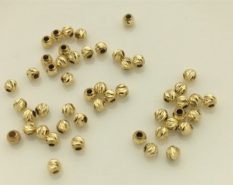May include: A collection of gold-colored round beads with a textured surface. The beads are scattered on a white surface.