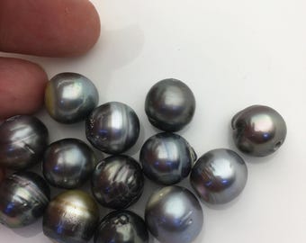 May include: A collection of twelve round, dark gray pearls with iridescent, metallic sheens. Each pearl displays a smooth, reflective surface with subtle variations in tone, ranging from deep charcoal to lighter silver-gray highlights.