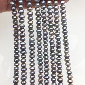 May include: Strands of dark gray freshwater pearls. The pearls have an oval shape and a lustrous finish. The pearls are strung together, creating a necklace or bracelet design. The pearls are a neutral color, suitable for various jewelry styles.