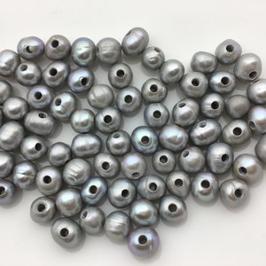 May include: A pile of gray pearl beads with holes for stringing. The pearls are a light gray color with a slight iridescent sheen.