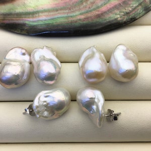 Può includere: Cinque perle barocche bianche, alcune con una leggera lucentezza iridescente, sono esposte su una superficie bianca. Due delle perle hanno perni per orecchini in argento.