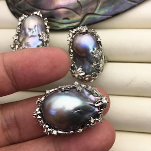 May include: Three rings featuring large, baroque-shaped, iridescent gray pearls set in silver with floral accents and small clear stones.