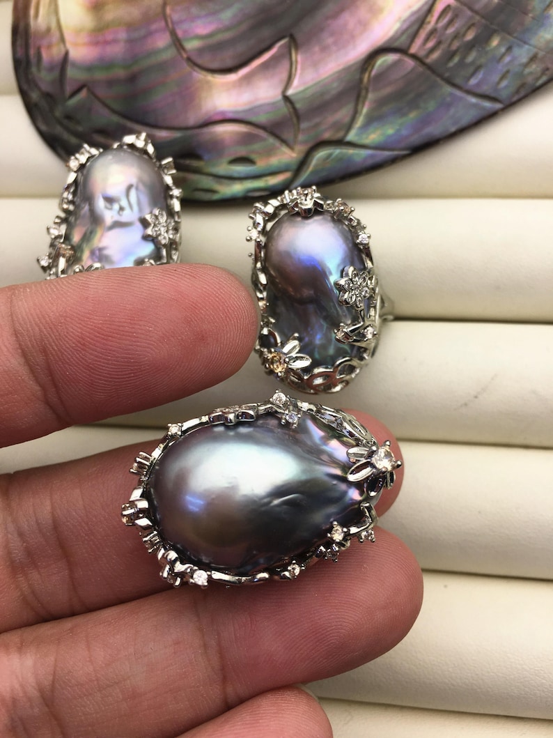 May include: Three rings featuring large, baroque-shaped, iridescent gray pearls set in silver with floral accents and small clear stones.