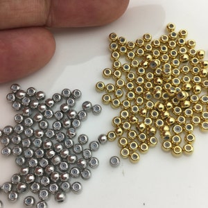 Puede incluir: Una imagen de primer plano de dos montones de cuentas redondas. Un montón es plateado y el otro es dorado.