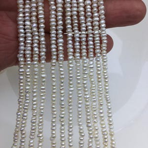 May include: A strand of white freshwater pearls, approximately 2-3mm in size, strung on a thin thread. The pearls are uniform in shape and have a smooth, lustrous finish.