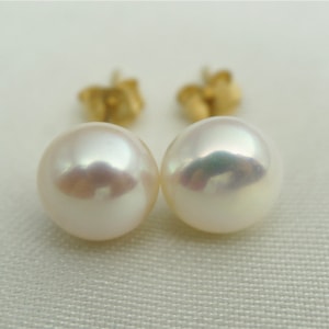 Op de afbeelding: Een paar witte parel oorbel studs met gouden pinnen. De parels zijn rond en hebben een gladde, glanzende afwerking.