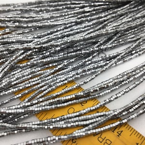 Könnte beinhalten: Eine Strähne silberfarbener quadratischer Perlen, etwa 4 mm groß, auf einem gelben Lineal ausgelegt. Die Perlen sind in Reihen angeordnet und gleichmäßig verteilt.