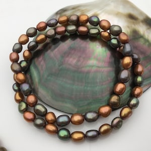 Può includere: Un filo di perle d'acqua dolce iridescenti marroni e nere. Le perle sono di forma ovale e hanno una finitura liscia e lucida.