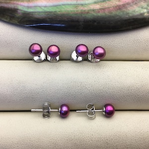 May include: A set of four purple pearl stud earrings. The earrings are displayed on a white surface.