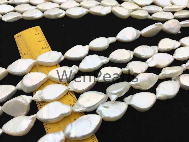 May include: A strand of white freshwater pearls with a slightly irregular, oval shape. The pearls are strung on a clear thread and are arranged in a loose, flowing pattern. The pearls are approximately 10mm in size.