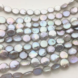 Puede incluir: Una hebra de perlas blancas e iridiscentes con forma de moneda. Las perlas son lisas y tienen una forma ligeramente irregular.