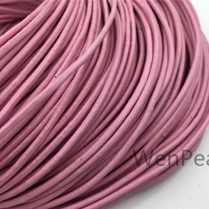 Puede incluir: Primer plano de un carrete de cordón de cuero rosa. El cordón es liso y tiene un ligero brillo. El cordón está enrollado apretado, creando una superficie densa y texturizada.