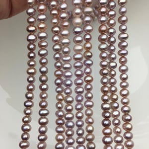May include: Several strands of lustrous, oval-shaped pearls in varying shades of pink and lavender. The pearls are strung together, creating a cascading effect. The pearls have a subtle sheen, reflecting light. Ideal for jewelry making or crafting.