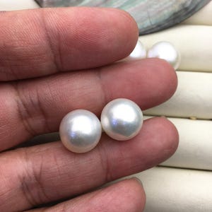 Op de afbeelding: Twee witte ronde parels, één in elke hand, tegen een witte achtergrond.