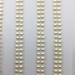 Puede incluir: Tres filas de perlas redondas blancas dispuestas verticalmente sobre un fondo blanco.