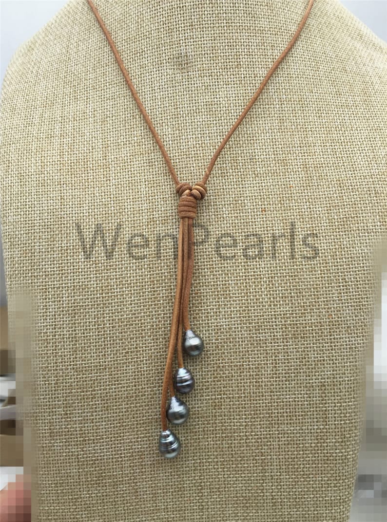 May include: A brown leather necklace with a knotted tassel and four dark gray pearls hanging from it.
