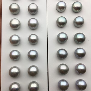 May include: A white card with two rows of 10 iridescent gray pearls. The pearls are arranged in a grid pattern on the card.