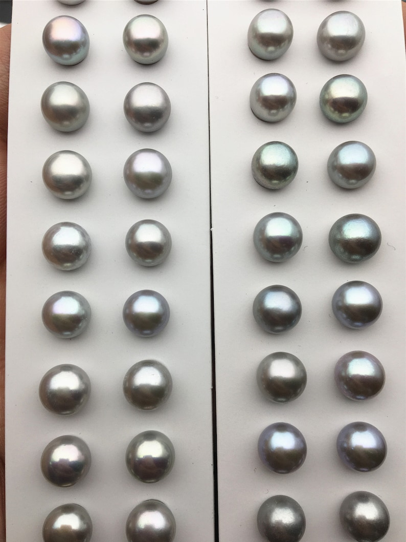 May include: A white card with two rows of 10 iridescent gray pearls. The pearls are arranged in a grid pattern on the card.