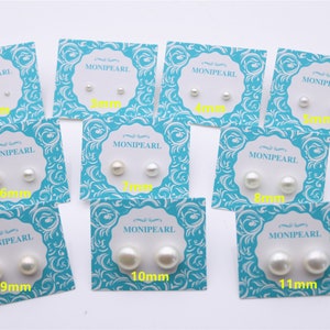 Puede incluir: Diez tarjetas con pendientes de perlas blancas sobre tarjetas con patrones azules y blancos. Las tarjetas están etiquetadas con el tamaño de las perlas en milímetros, que van de 2 mm a 11 mm. La marca "MONIPEARL" está impresa en cada tarjeta.