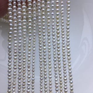 May include: A strand of white freshwater pearls, approximately 4-5mm in size, strung on a thin thread. The pearls are round and smooth, with a slight iridescent sheen.