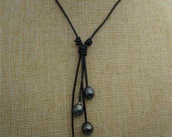 May include: A black leather necklace with a knotted design and four black pearls hanging from the bottom.