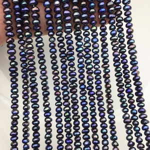 Può includere: Molteplici fili di piccole perle d'acqua dolce rotonde di colore viola scuro. Ogni perla presenta una lucentezza iridescente con sottili sfumature di blu e verde. Le perle sono infilate in lunghe linee verticali, mostrando dimensioni e forma uniformi.