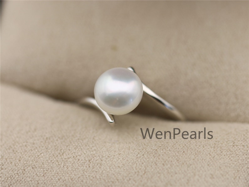 May include: A silver ring with a white pearl set in a simple, curved band. The ring is on a beige background. WenPearls is written in the bottom right corner of the image.