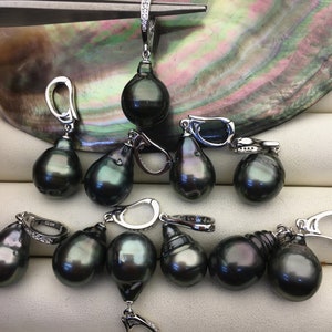 May include: A set of ten black pearl earrings with silver clasps. The pearls are teardrop shaped and have a dark green hue. The earrings are displayed on a black and white surface.