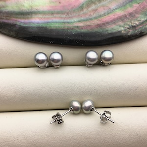 Könnte beinhalten: Ein Paar silberne Perlmutt-Ohrstecker. Die Perlen sind rund und glatt, und die Ohrringe sind in Silber gefasst.