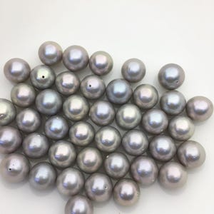 May include: A collection of lustrous, round, gray pearls with iridescent surfaces. The pearls vary slightly in size and have a smooth, polished appearance. Some pearls have small holes, indicating they are ready for stringing.