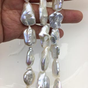 May include: Three strands of white baroque pearls with an irregular, organic shape and a high-luster, iridescent finish. Each pearl displays unique ridges and smooth, reflective surfaces that catch the light, creating a shimmering effect.