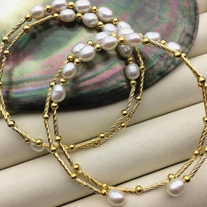 May include: A double strand gold chain bracelet with white pearls. The bracelet is made of two twisted chains with small gold beads between each pearl.