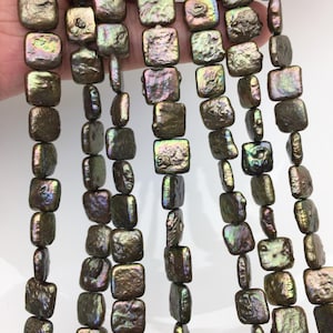 May include: Strands of iridescent, square-shaped beads in shades of bronze, green, and purple. The beads have a textured surface and are strung together, creating a shimmering effect. The beads are likely used for jewelry making.