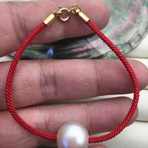 May include: A red string bracelet with a gold clasp and a large white pearl.