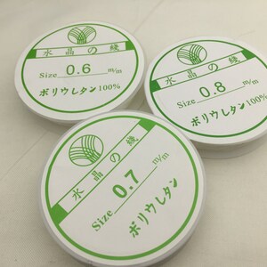 May include: Three white spools of clear fishing line with green labels. The labels have Japanese text and say "Size 0.6 m/m, Size 0.7 m/m, and Size 0.8 m/m". The labels also say "Polyurethane 100%".