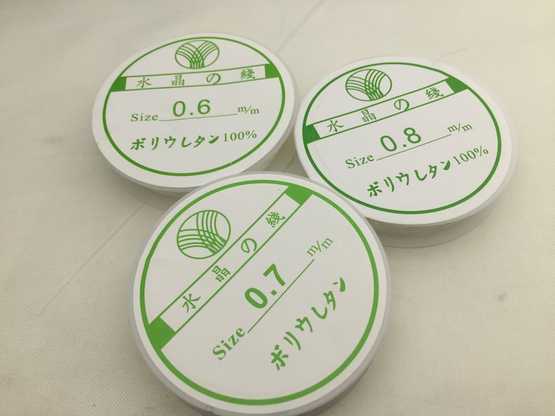 May include: Three white spools of clear fishing line with green labels. The labels have Japanese text and say "Size 0.6 m/m, Size 0.7 m/m, and Size 0.8 m/m". The labels also say "Polyurethane 100%".